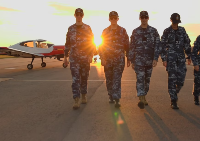 Image of cadets walking in front of an aircraft with the sun setting behind.